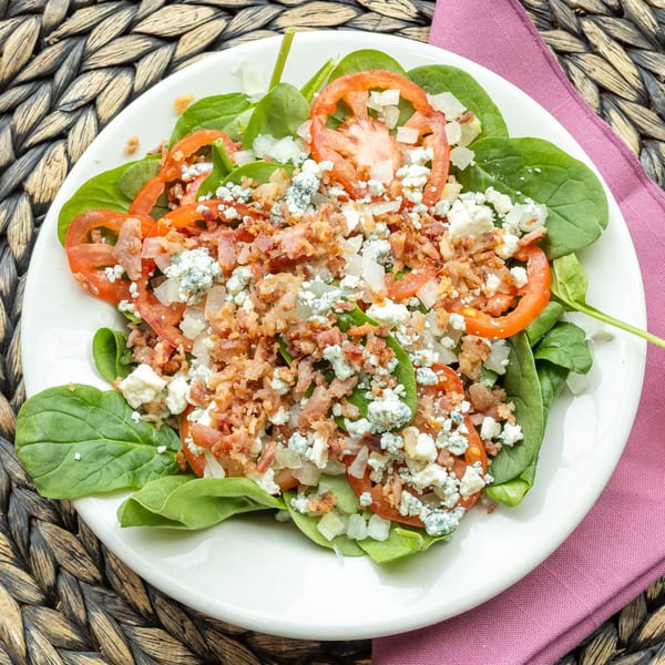 Spinach salad with sliced tomatoes, crumbled bacon, diced onions, and blue cheese crumbles.