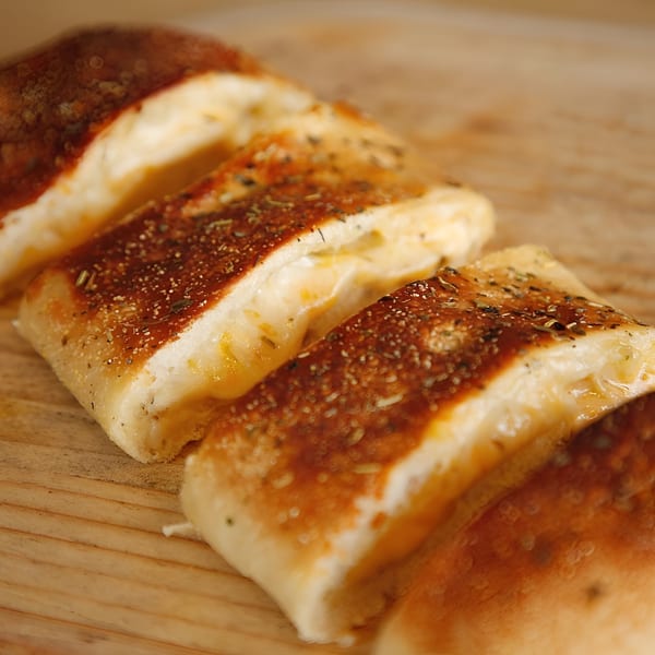 Four golden-brown Mama Mimi's cheesy breadsticks, seasoned with herbs, on a wooden surface.