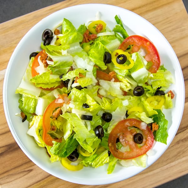 Fresh garden salad with lettuce, tomatoes, black olives, and banana peppers in a white bowl.