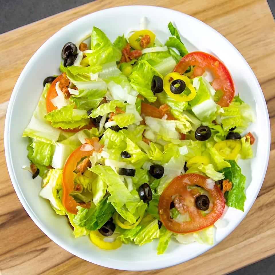 Fresh garden salad with lettuce, tomatoes, black olives, and banana peppers in a white bowl.