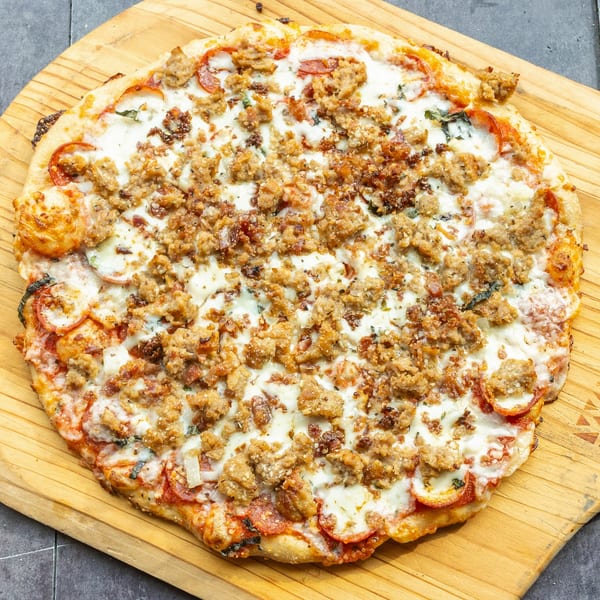 A Mama Mimi's Take 'N Bake Pizza with pepperoni, sausage, and cheese on a wooden peel.