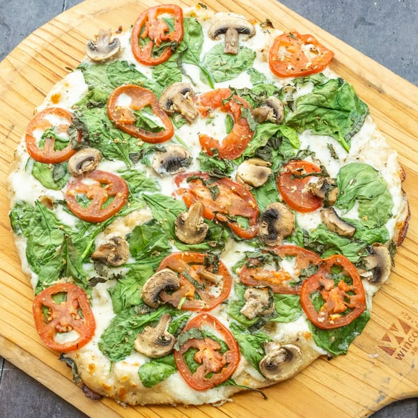 Mama Mimi's white pizza with spinach, sliced tomatoes, and mushrooms on a wooden peel.
