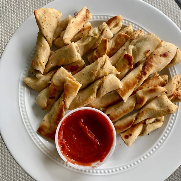 Twisted breadsticks seasoned with herbs and cheese, served with a side of red marinara sauce.