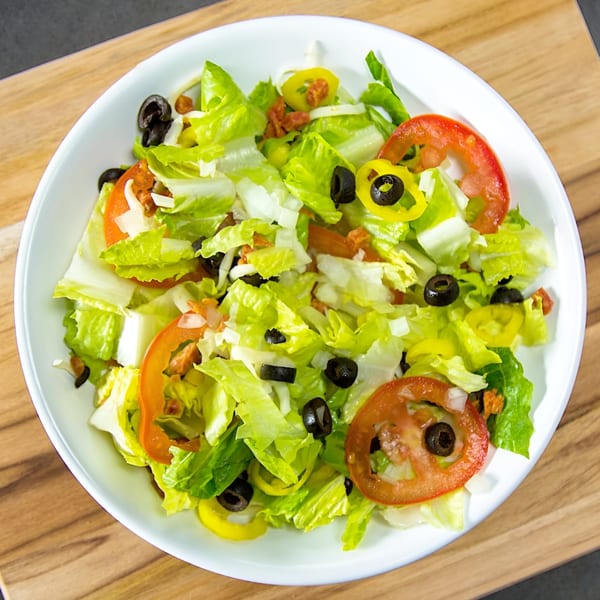 Fresh garden salad with crisp lettuce, sliced tomatoes, black olives, and banana peppers in a white bowl.