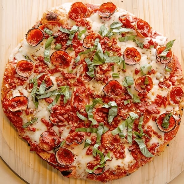 A Mama Mimi's Take 'N Bake pepperoni pizza, topped with fresh basil, on a wooden peel.
