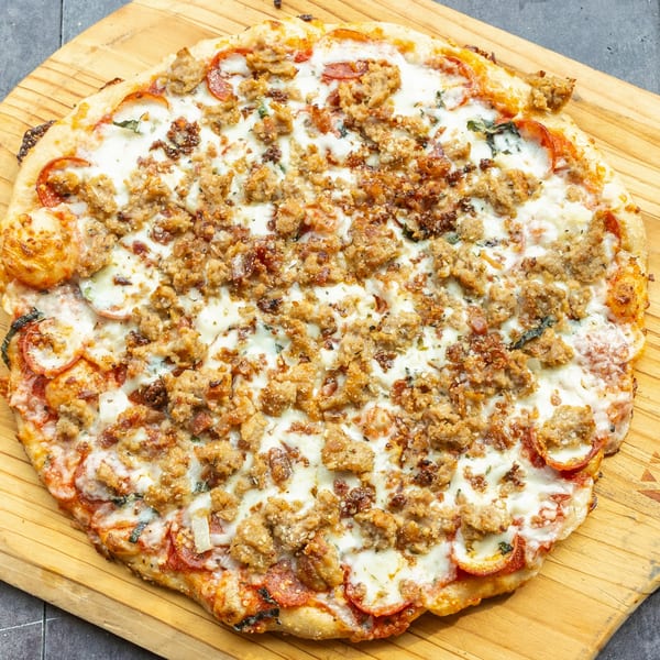 Mama Mimi's Take 'N Bake Pizza with pepperoni, sausage, and melted cheese on a wooden board.