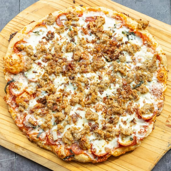 Mama Mimi's Take 'N Bake Pizza with pepperoni, sausage, and melted cheese on a wooden board.